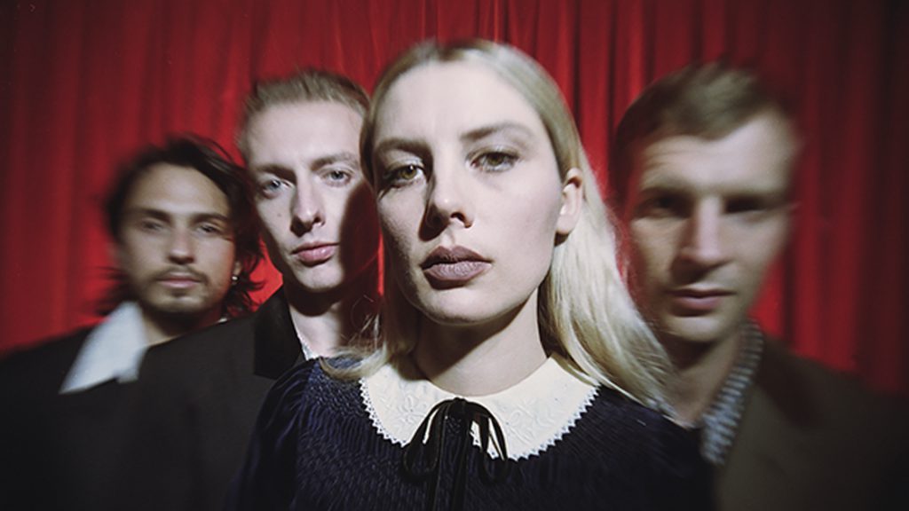 Photo of Wolf Alice members in front of red curtain