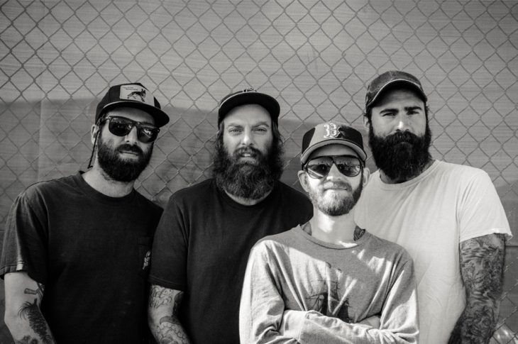 Black & white photo of members of Four Year Strong in front of chain link fence.