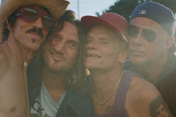 Photo of members of Red Hot Chili Peppers hugging outside in the sun