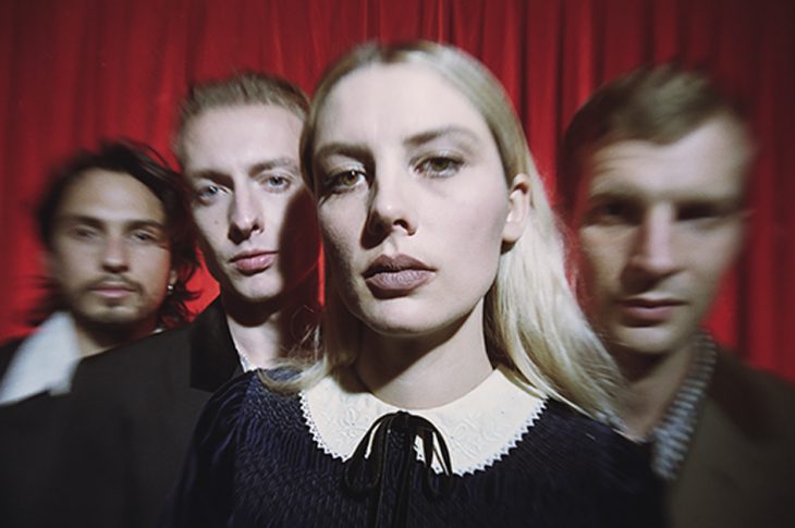 Photo of Wolf Alice members in front of red curtain