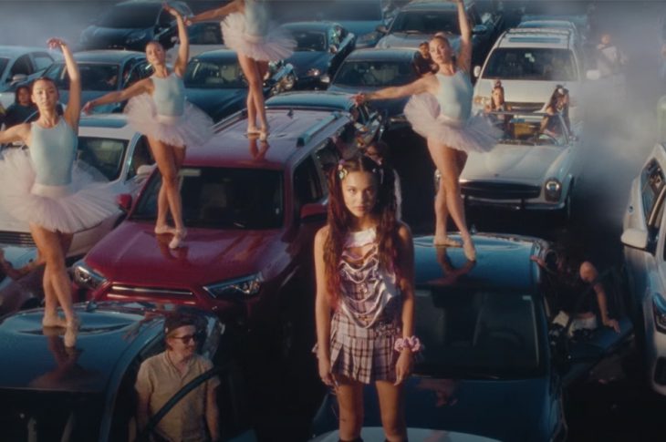 video still of Olivia Rodrigo standing on top of a guitar in a traffic jam