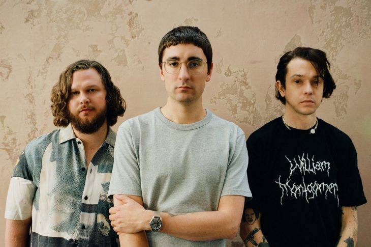 Photo of Alt. J band members in front of beige wall by George Muncie.