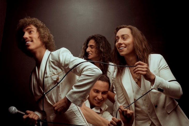 Greta Van Fleet band members tangled up in microphone cord while wearing white suits. Photo by Alysse Gafkjen