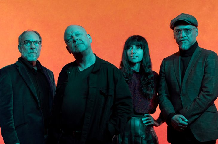 Photo of Pixies band members standing in front of orange backdrop