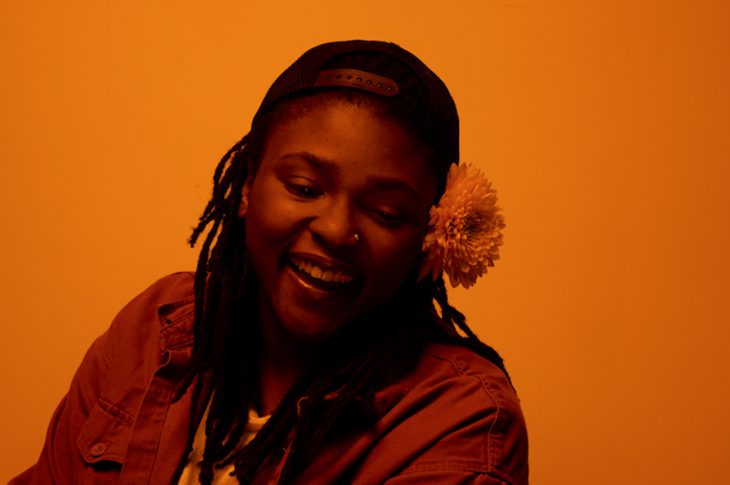Orange tinted photo of Joy Oladokun smiling wearing baseball hat.