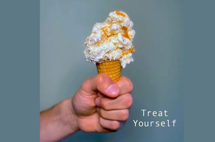 Image of hand holding ice cream cone against blue background