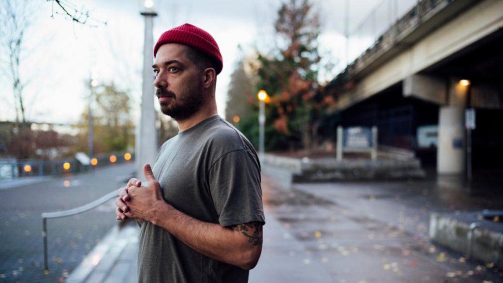 Aesop Rock standing on city street.