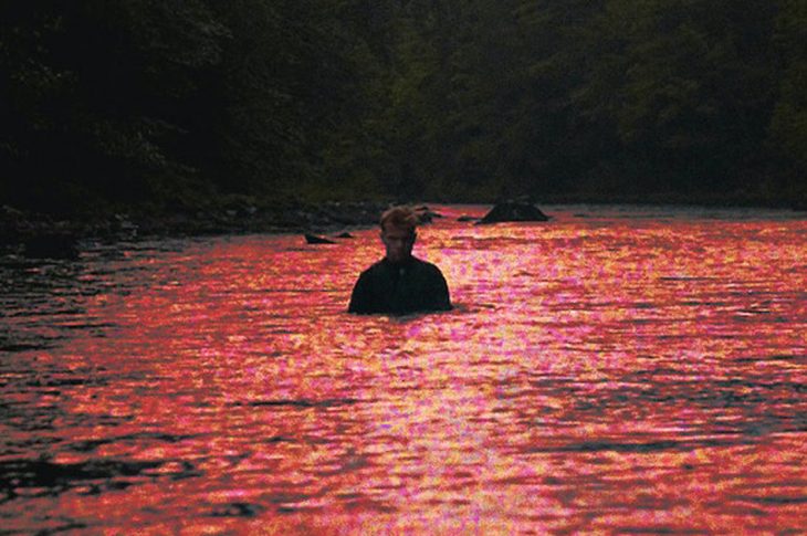 red hued picture of man standing in river.