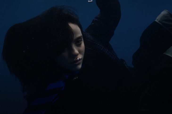 Billie Eilish dressed in black, underwater, photographed against blue background