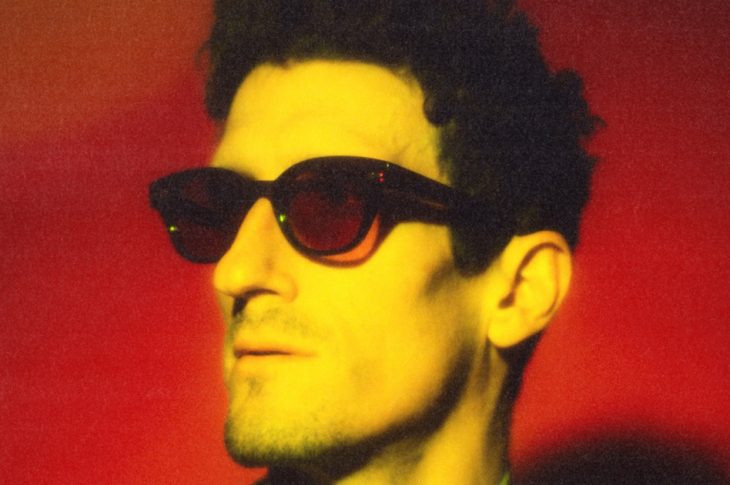 mans wearing sunglasses photographed against red background