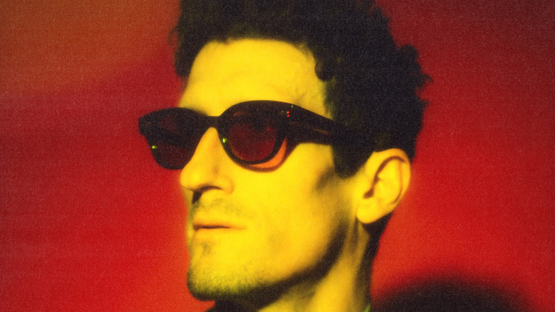 mans wearing sunglasses photographed against red background