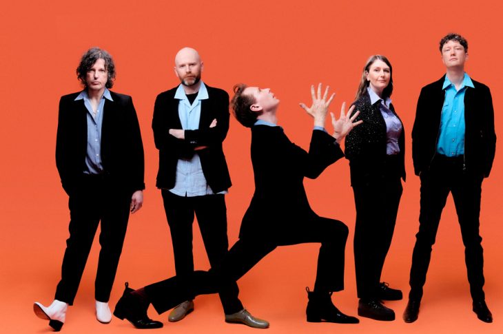 5 people dressed in black photographed against orange background