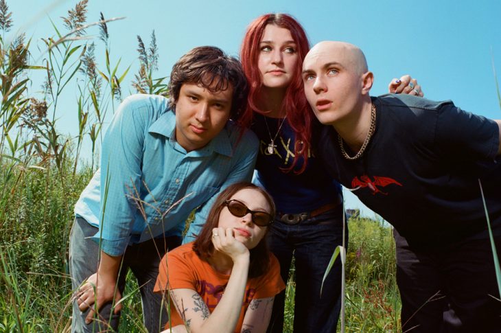 4 people standing in tall grass on sunny day.