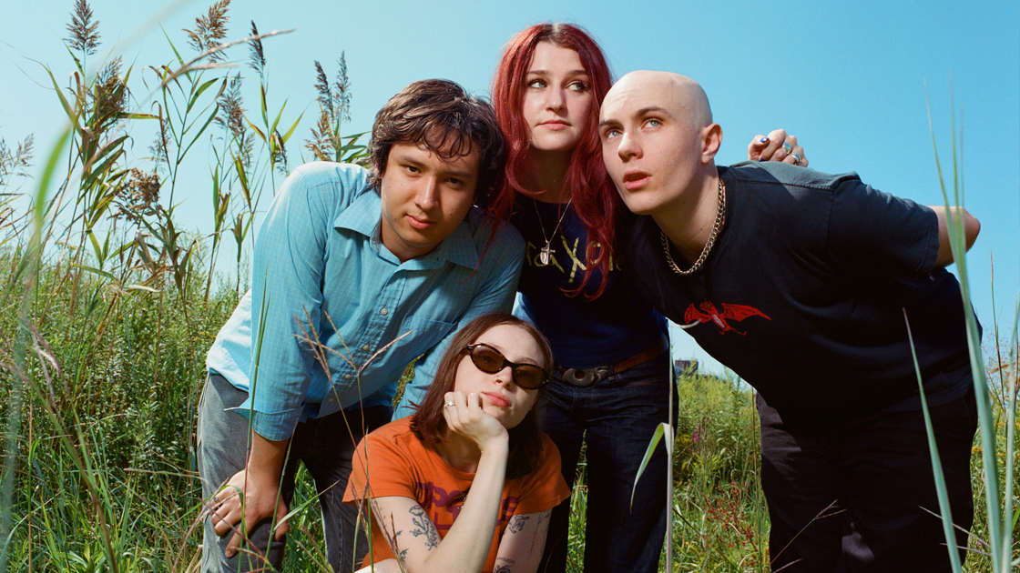 4 people standing in tall grass on sunny day.