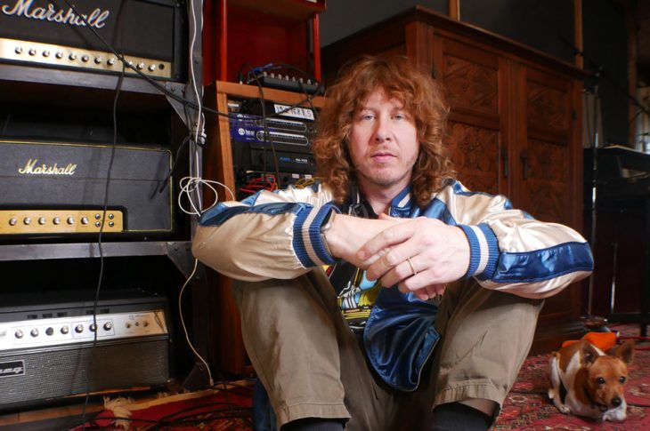 photo of man sitting on the floor of recording studio with small dog