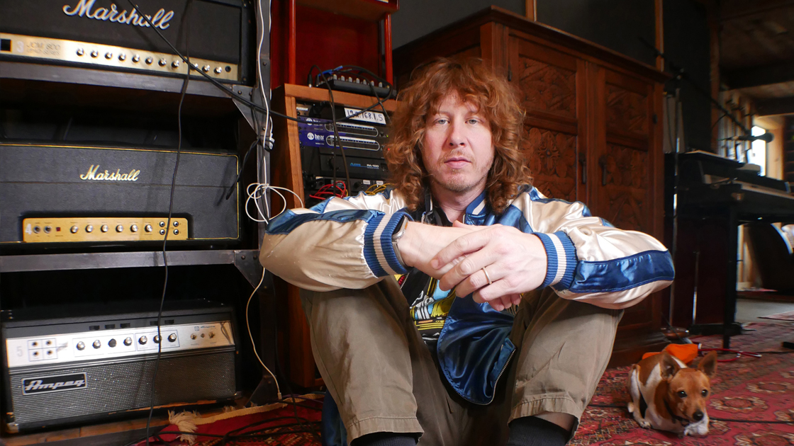 photo of man sitting on the floor of recording studio with small dog