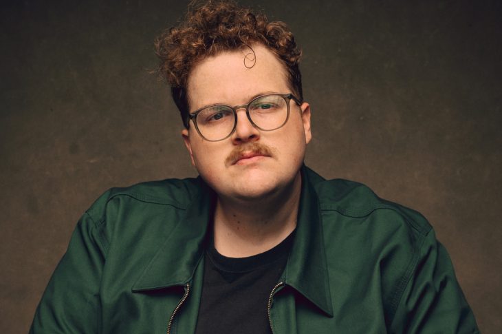 Photo of man with curly hair and mustache in green shirt