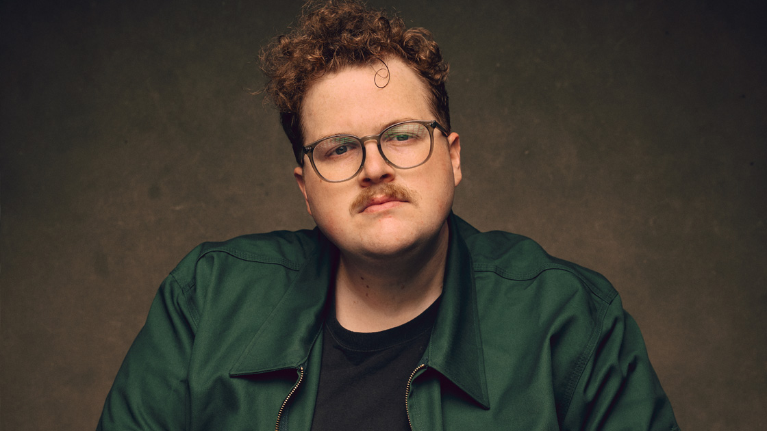 Photo of man with curly hair and mustache in green shirt