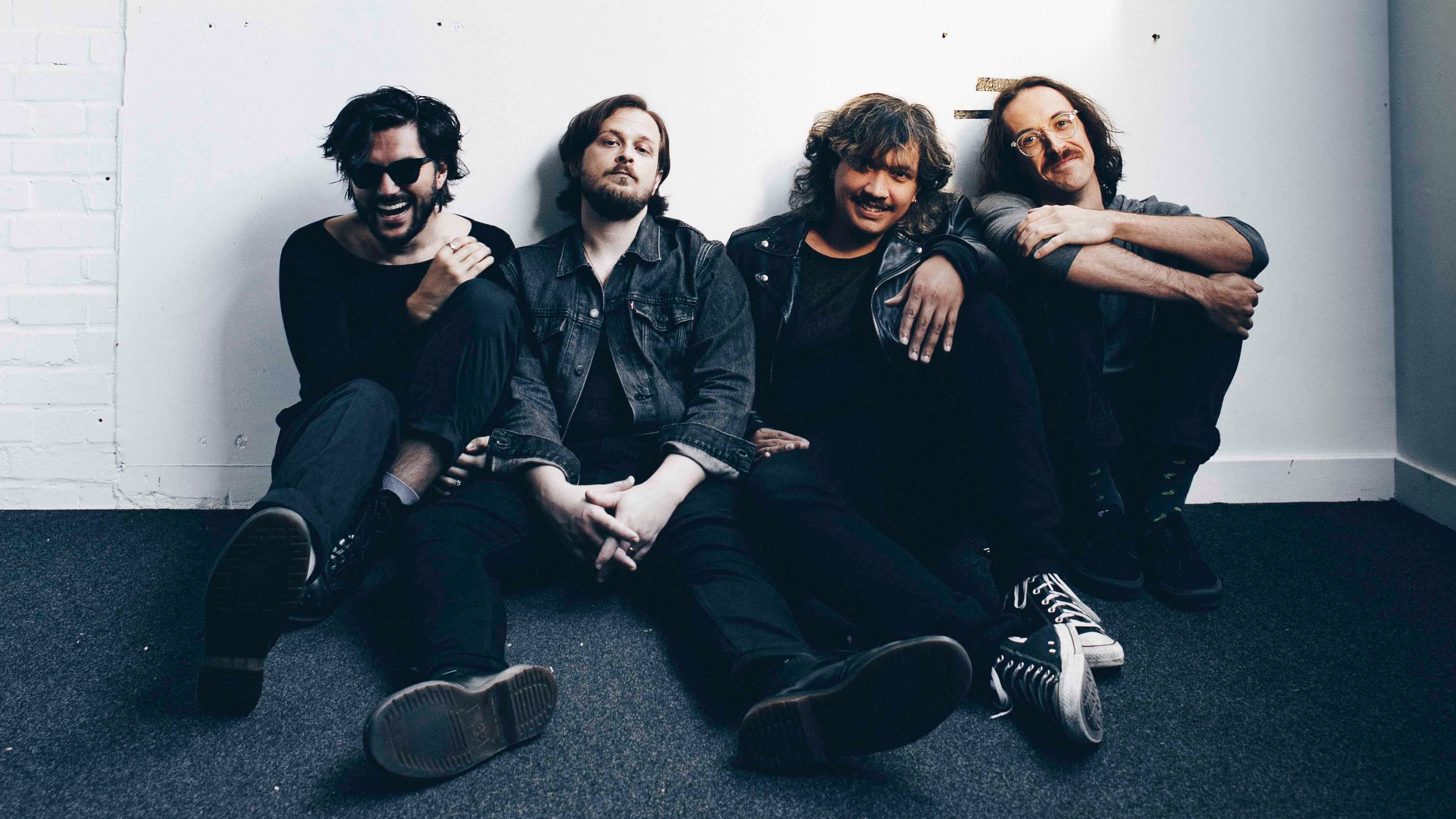 Four men sitting on the floor against white wall.