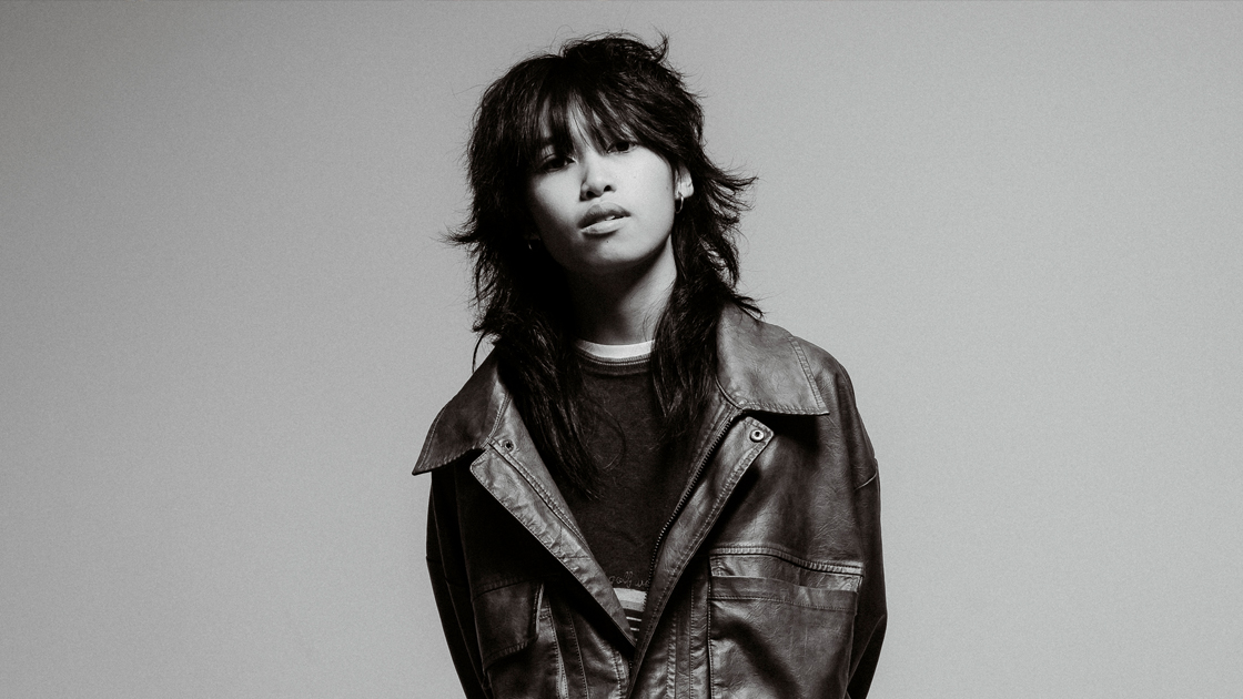 Black and white photo of artist in leather jacket against white backdrop