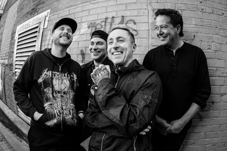 black & white photo of 4 men photographed against brick wall