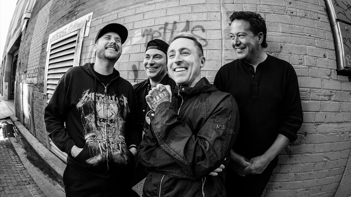 black & white photo of 4 men photographed against brick wall