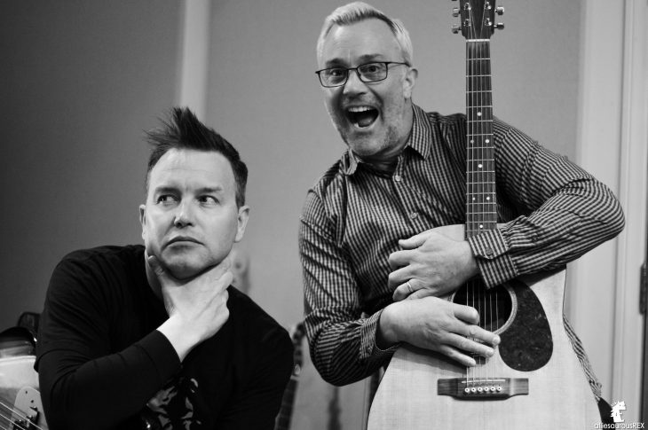 black and white photo of two men. One is holding a guitar.