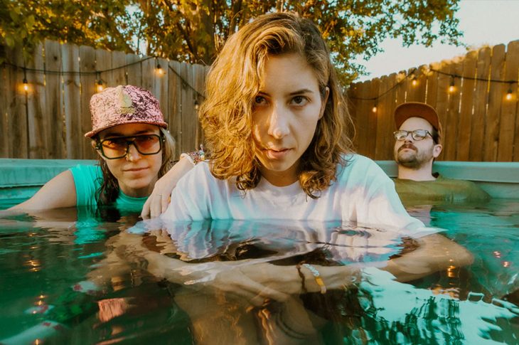 three people sitting fully clothed in a pool.