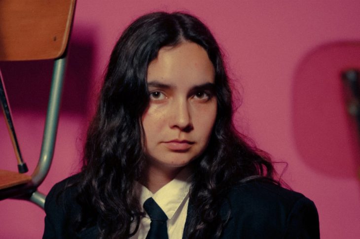 Photo of woman in black suit and tie in front of pink background