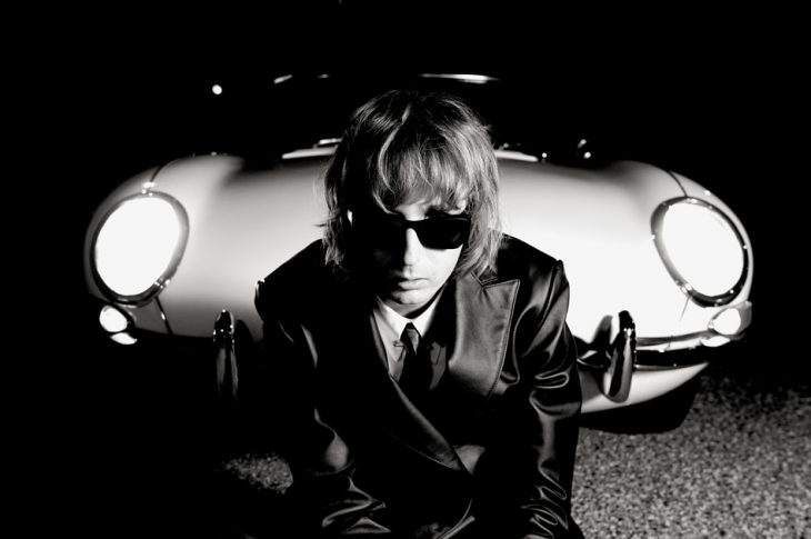 black and white of man wearing sunglasses sitting in front of car