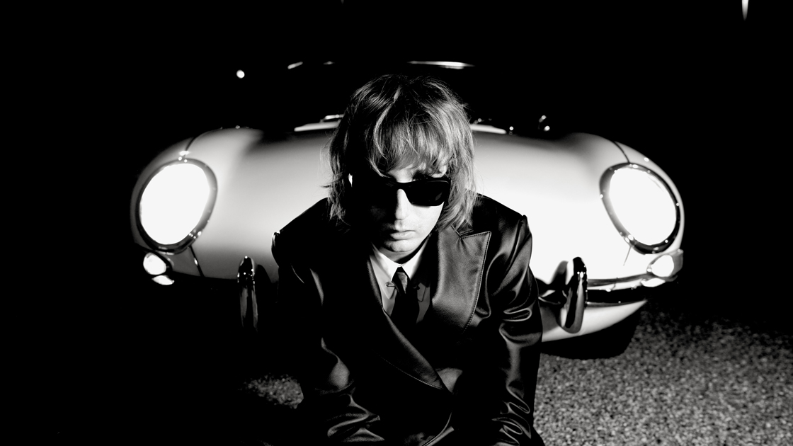 black and white of man wearing sunglasses sitting in front of car