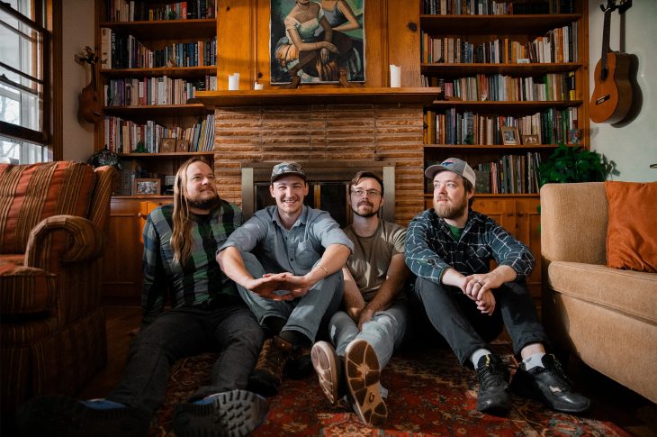 Four men sitting on the floor of a den.
