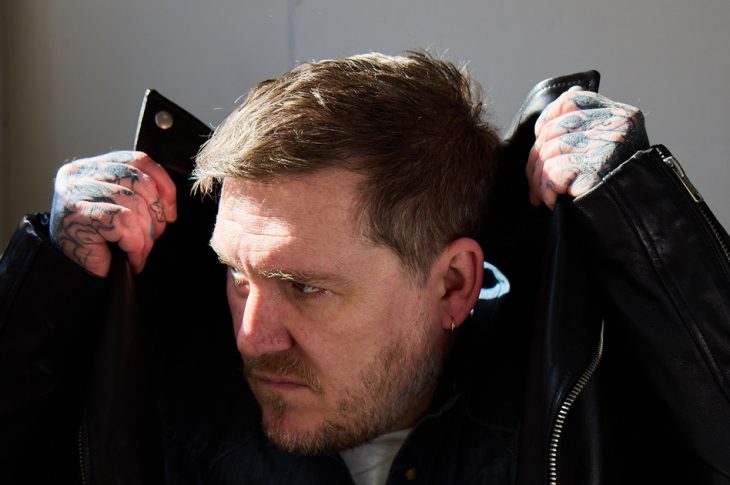Man wearing leather jacket holding collar above his head.