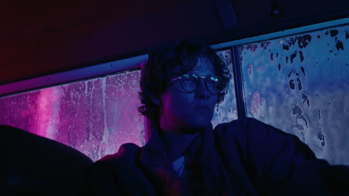 man sitting in car at night bathed in purple light.
